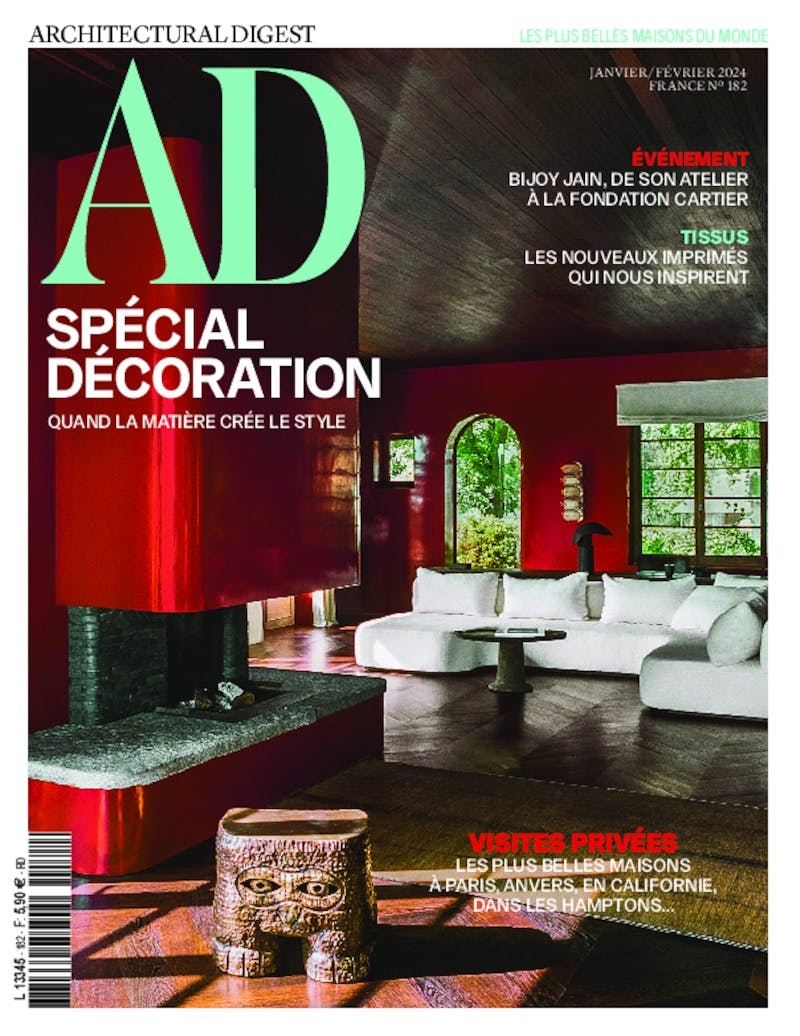 January/February 2024 cover of Architectural Digest France with a mint green 'AD' logo and the special feature 'SPÉCIAL DÉCORATION.' The visual showcases a stylish room with bold red walls, a modern white sofa, and a striking dark stone fireplace. Overlay text promotes private tours of the world's most beautiful homes, including in Paris, Antwerp, California, and the Hamptons.