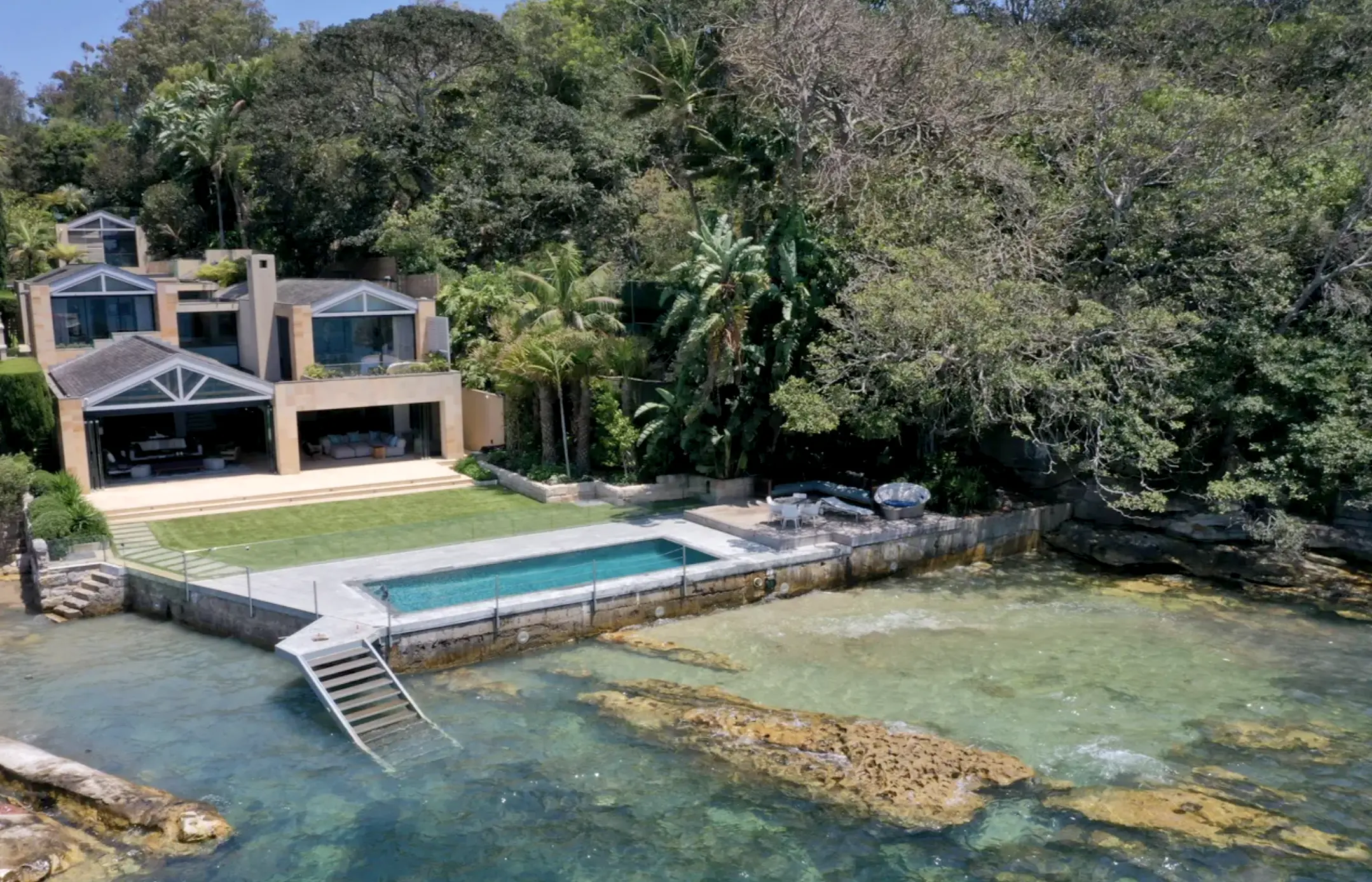 "Stunning waterfront estate designed by Nina Maya Interiors, nestled among lush greenery with direct access to the ocean. The multi-level home features expansive glass windows, modern architectural lines, and an open-concept design that seamlessly blends indoor and outdoor living. A luxurious infinity pool overlooks the crystal-clear waters, with a private sun deck and a staircase leading directly into the sea.